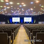 Image: Large auditorium at Allianz MiCo in Milan with tiered seating, dual presentation screens and integrated Yamaha Pro Audio sound system for conferences and events.